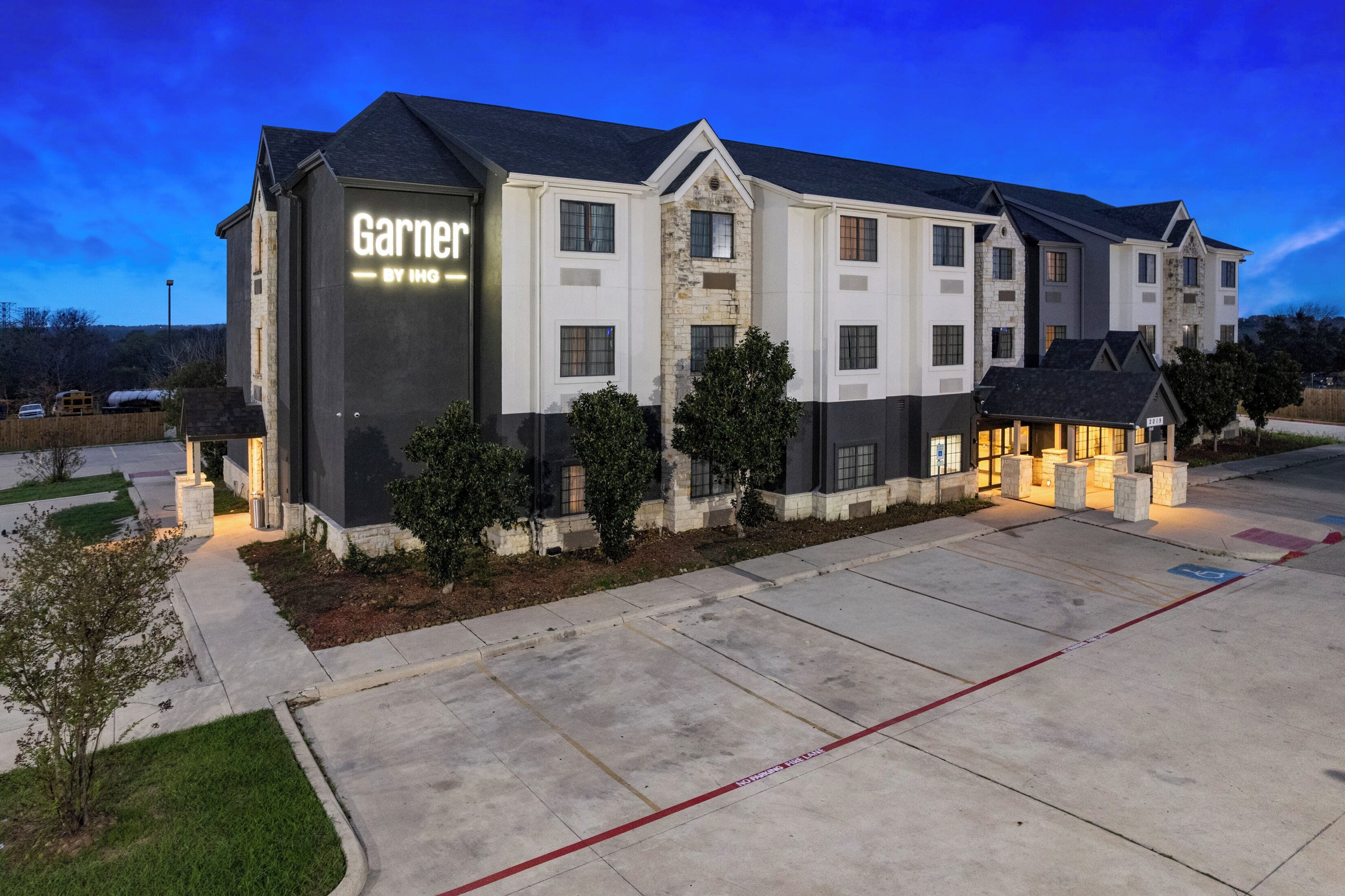 A multi-story hotel with a prominent 'Garner' sign, a driveway, and a landscaped area with trees.