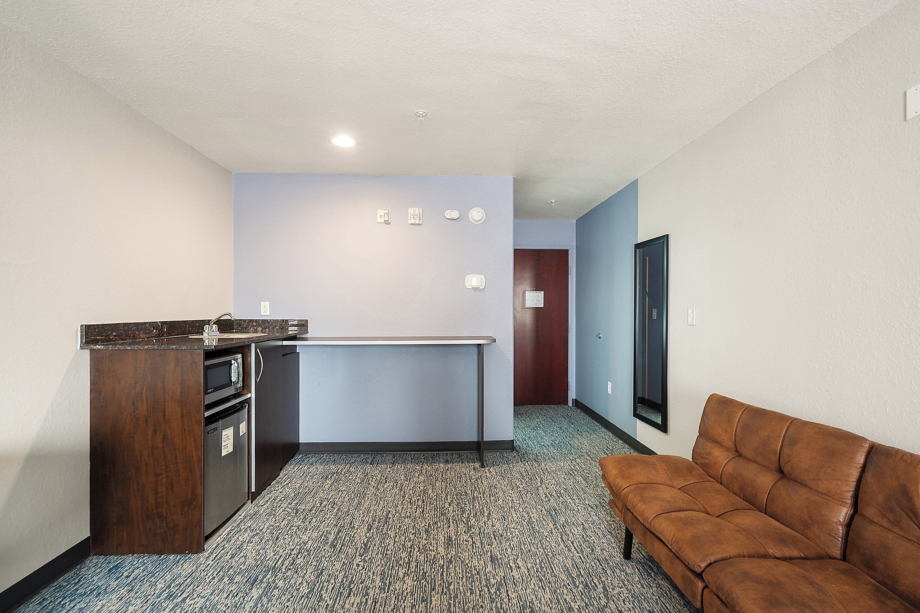 A compact living space with a kitchenette, a brown leather sofa, and a carpeted floor.