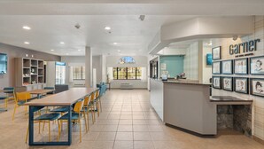 A hotel lobby with a long reception desk, a seating area with tables and chairs, and a view of the outdoors through a large window. - Garner Hotel Gonzales by IHG (Gonzales)