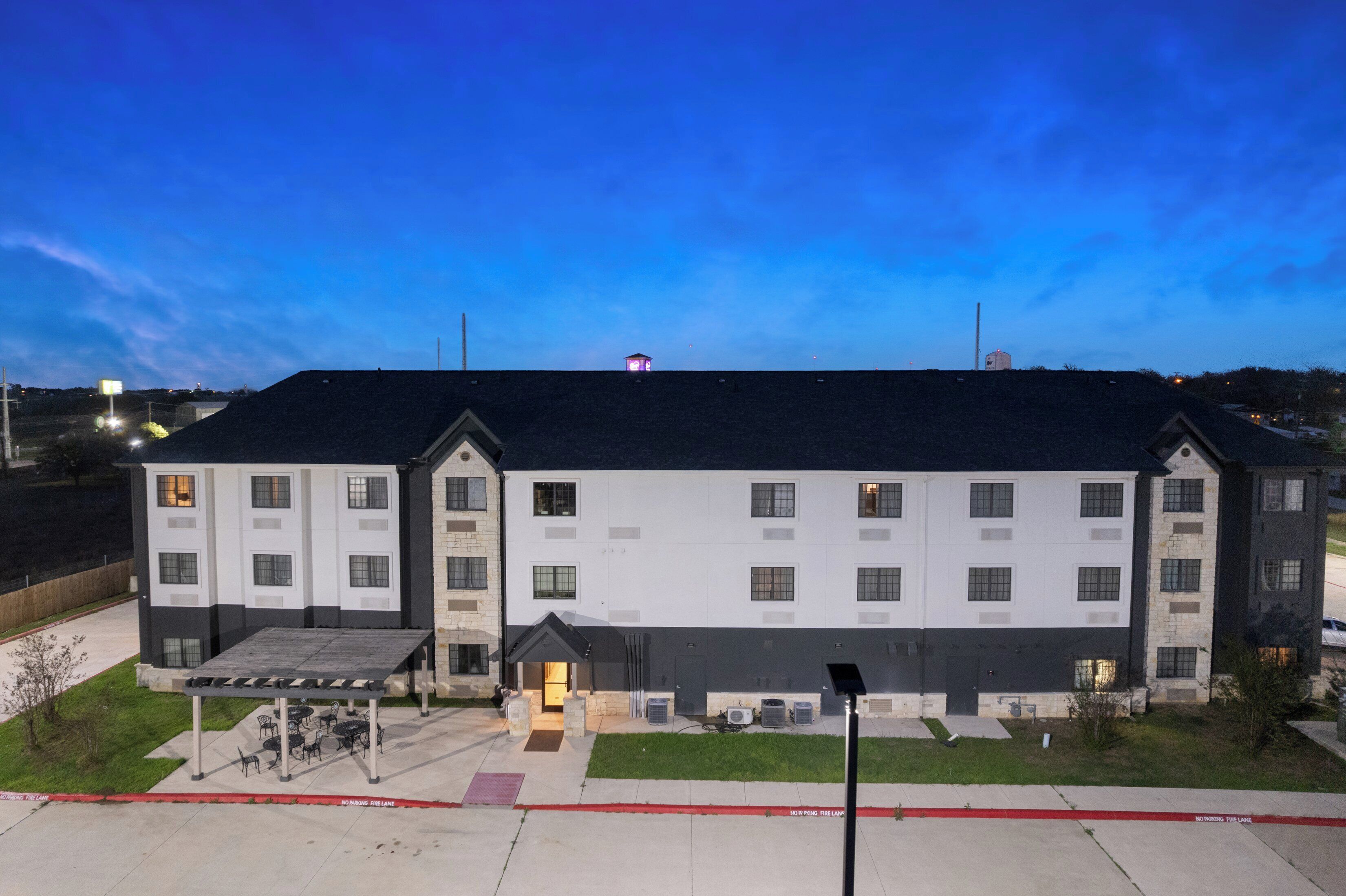 Un hotel de varios pisos con techo plano, un área de estar exterior cubierta e iluminación en la entrada.