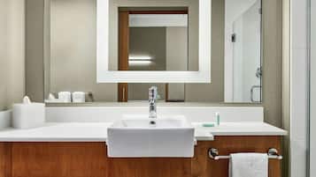 Un baño con lavamanos blanco, tocador de madera y un espejo sobre el lavamanos.