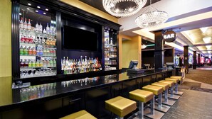 Un área de bar con una barra alargada, varios taburetes y una amplia variedad de botellas en estanterías.