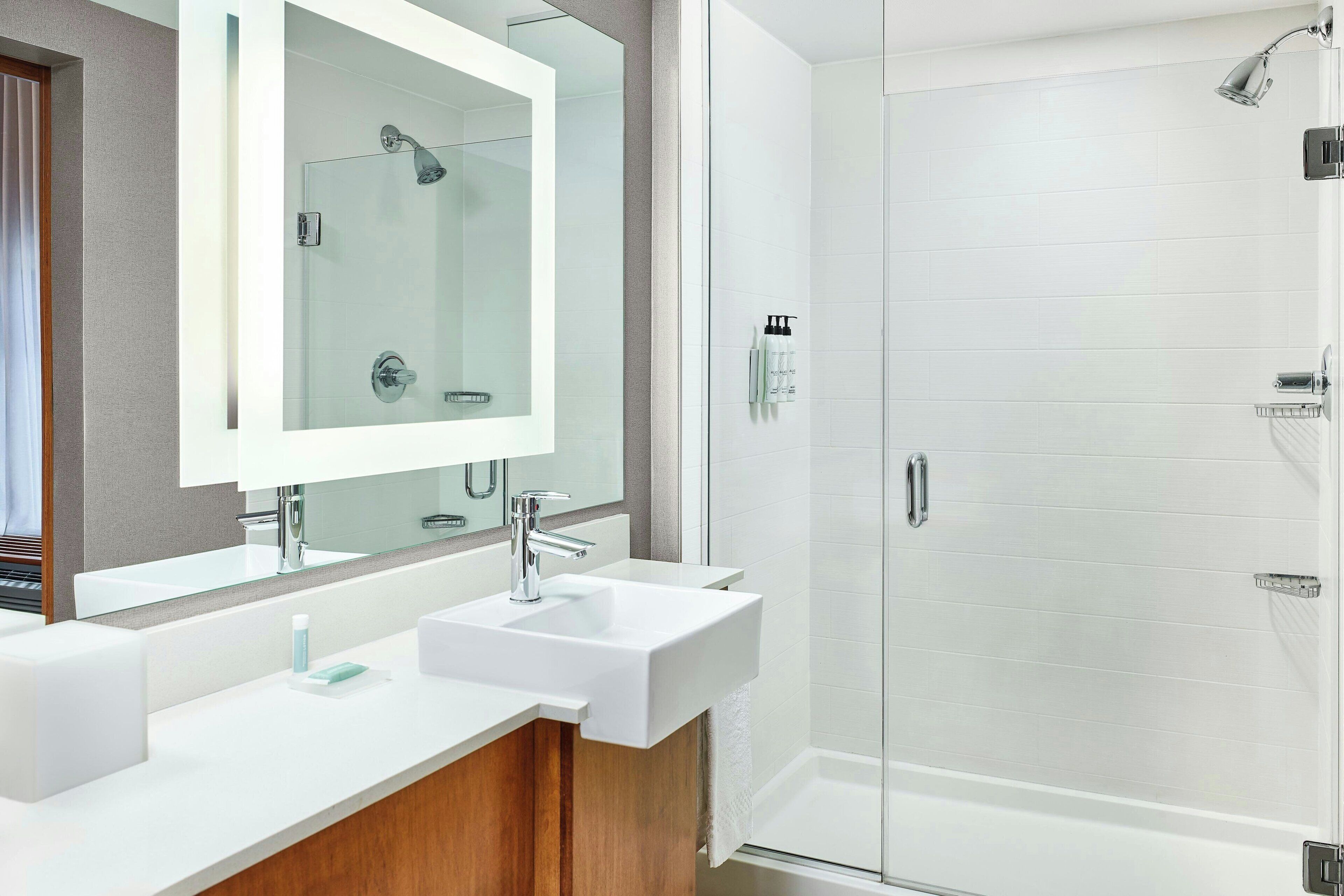 Une salle de bain moderne avec un grand miroir, deux lavabos, une douche et un espace douche fermé par des parois de verre.