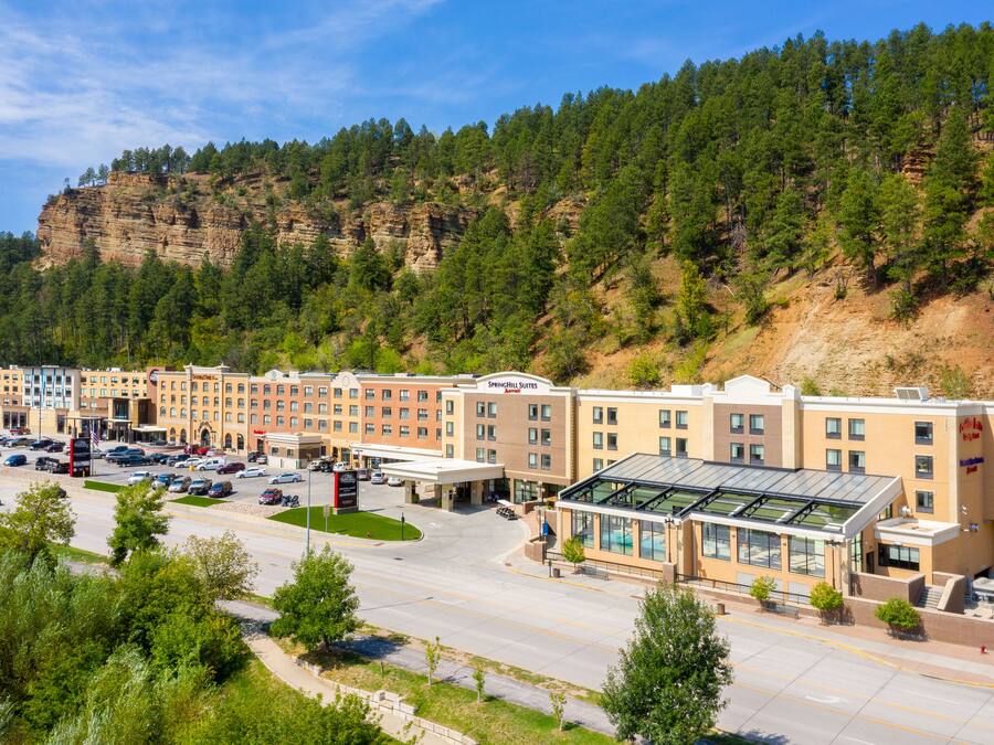 Un hotel con varias edificaciones, estacionamiento y montañas al fondo.