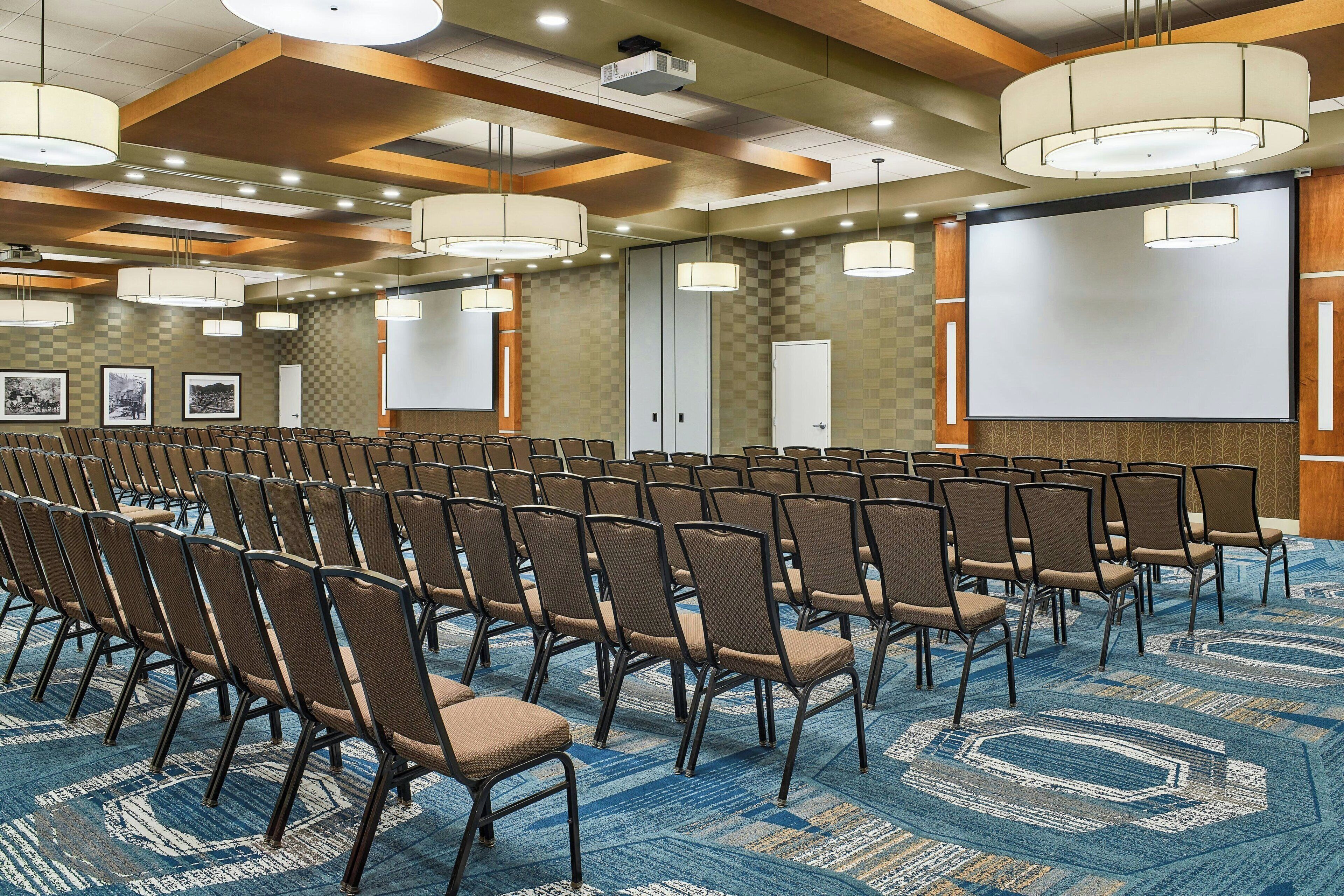 A conference room with rows of chairs, a large screen, and a carpeted floor.
