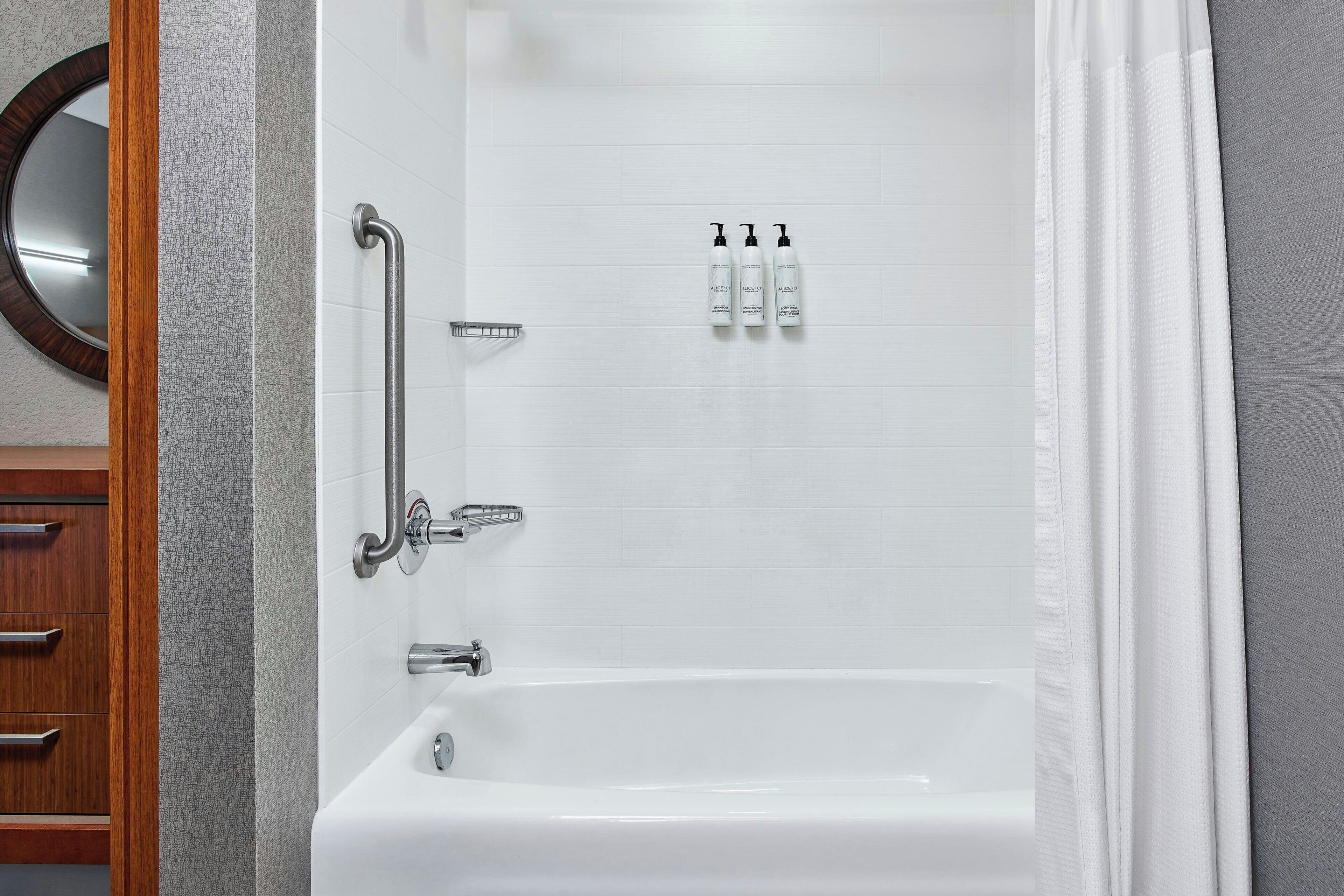 Un baño con bañera, barra de apoyo, toallero y tres botellas de champú.