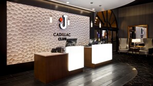 Una recepción con el letrero Cadillac Club, un diseño moderno con pared texturizada, y una zona de estar con una lámpara.