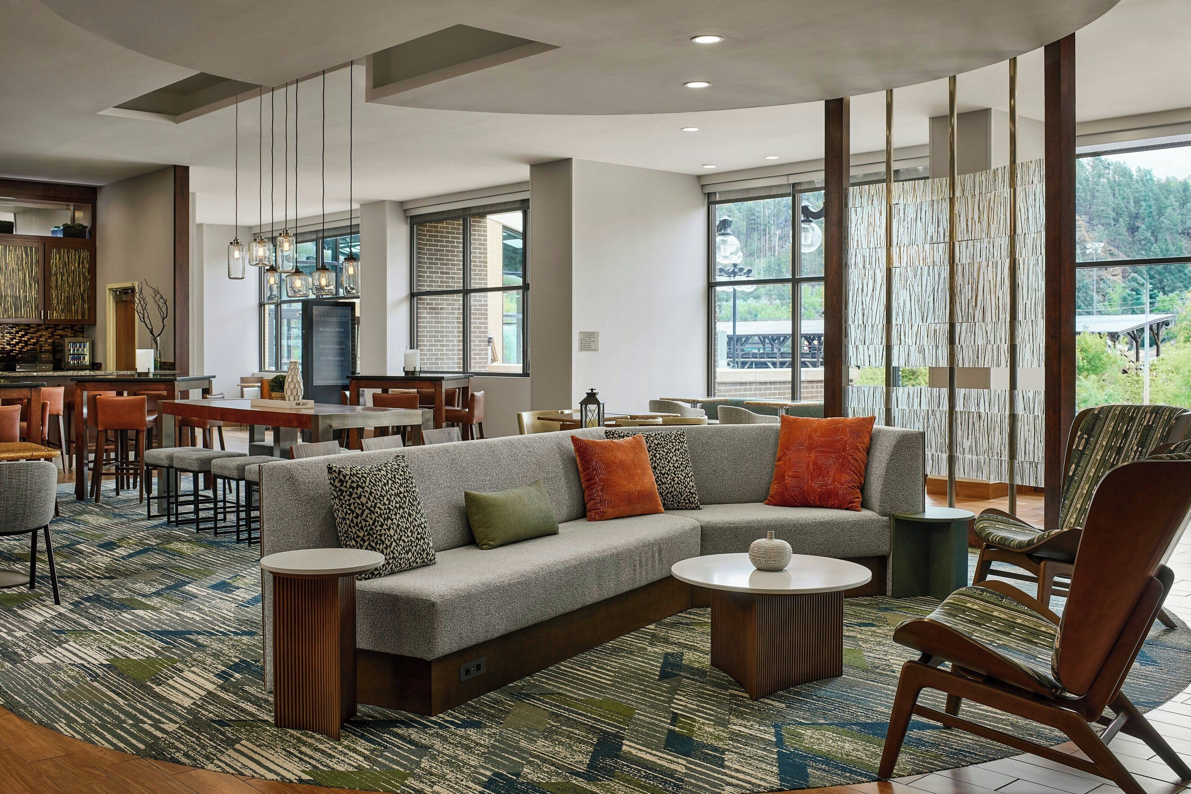 A modern lounge area with a sectional sofa, armchairs, and a coffee table. There are multiple seating options and a large window providing a view of the outdoors.