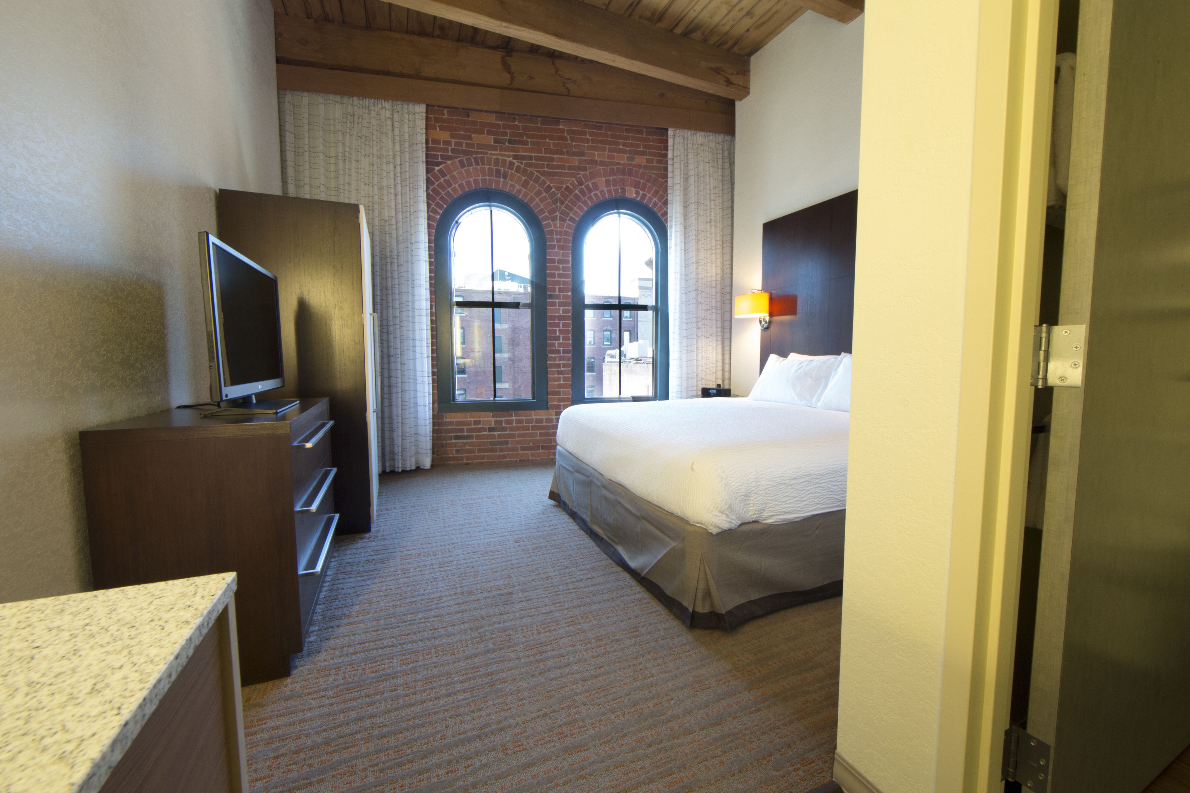 Een hotelkamer met een bed, een televisie, een bureau en een raam met uitzicht op een bakstenen muur.