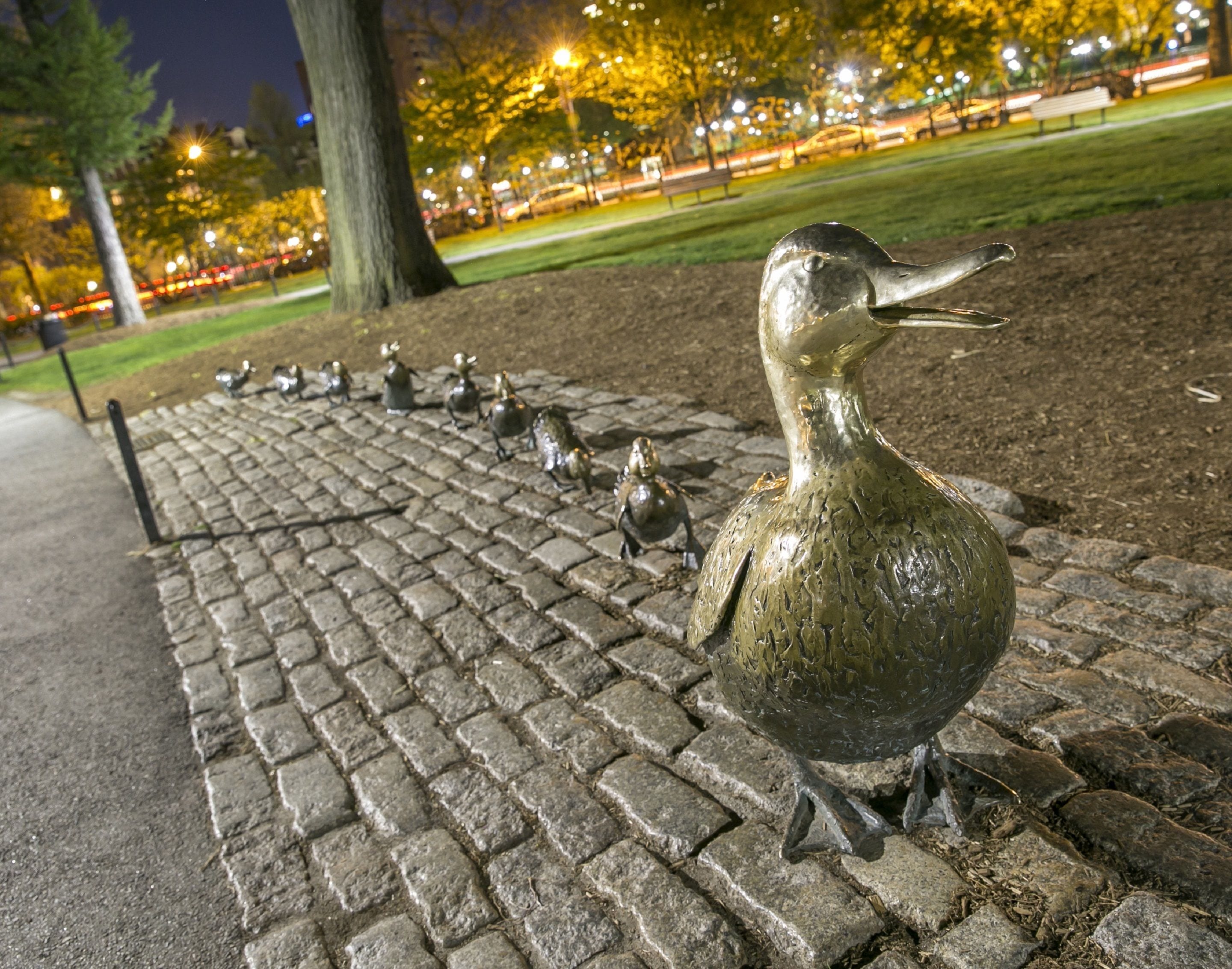 Une rangée de sculptures d’oiseaux le long d’une allée pavée dans un parc, de nuit.