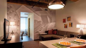 A modern hotel room with a dining area, a sofa, a TV, and a desk.