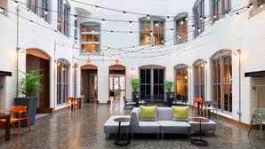 A spacious indoor area with a central seating area, multiple tables, and chairs, surrounded by white brick walls and large windows. - Residence Inn by Marriott Boston Downtown/Seaport (Boston)