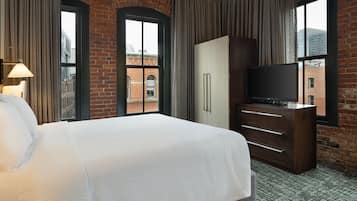 Une chambre d’hôtel avec un grand lit, une armoire, un téléviseur et une vue sur un immeuble en briques, visible par la fenêtre.
