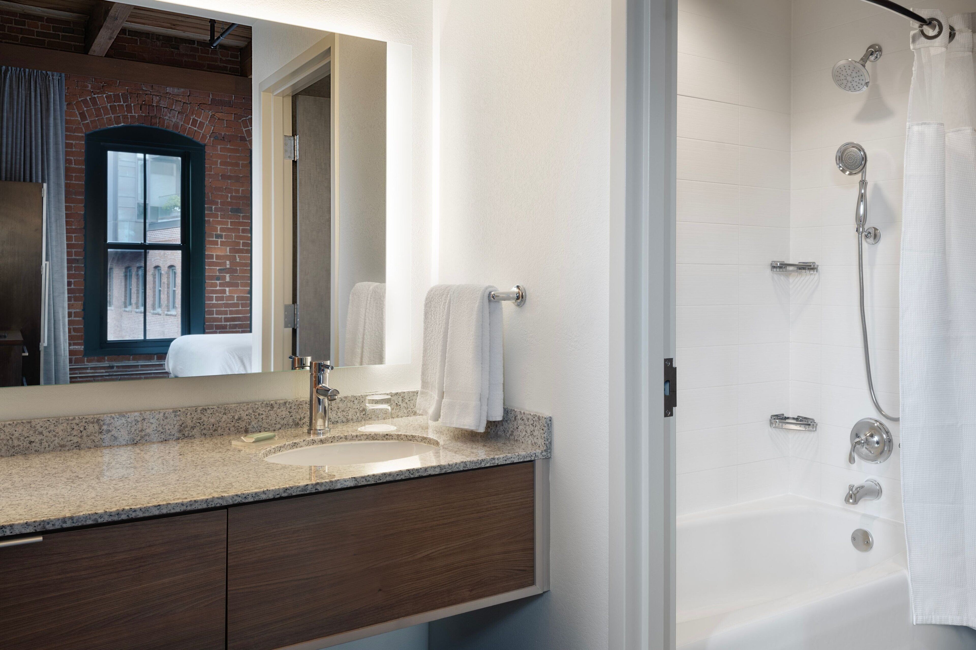 A modern bathroom with a granite countertop sink, a large mirror, and a walk-in shower with a glass door.