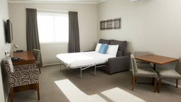 A hotel room with a bed, a desk, a chair, a table, and a TV.