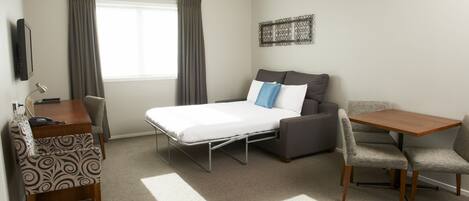 A hotel room with a bed, a desk, a chair, a table, and a TV.