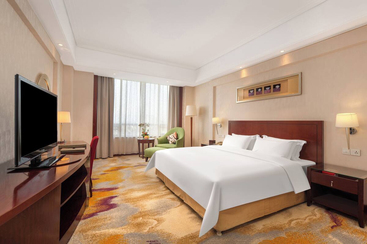 Ein Hotelzimmer mit einem großen Bett, einem Fernseher, einem Schreibtisch und einem Sessel.