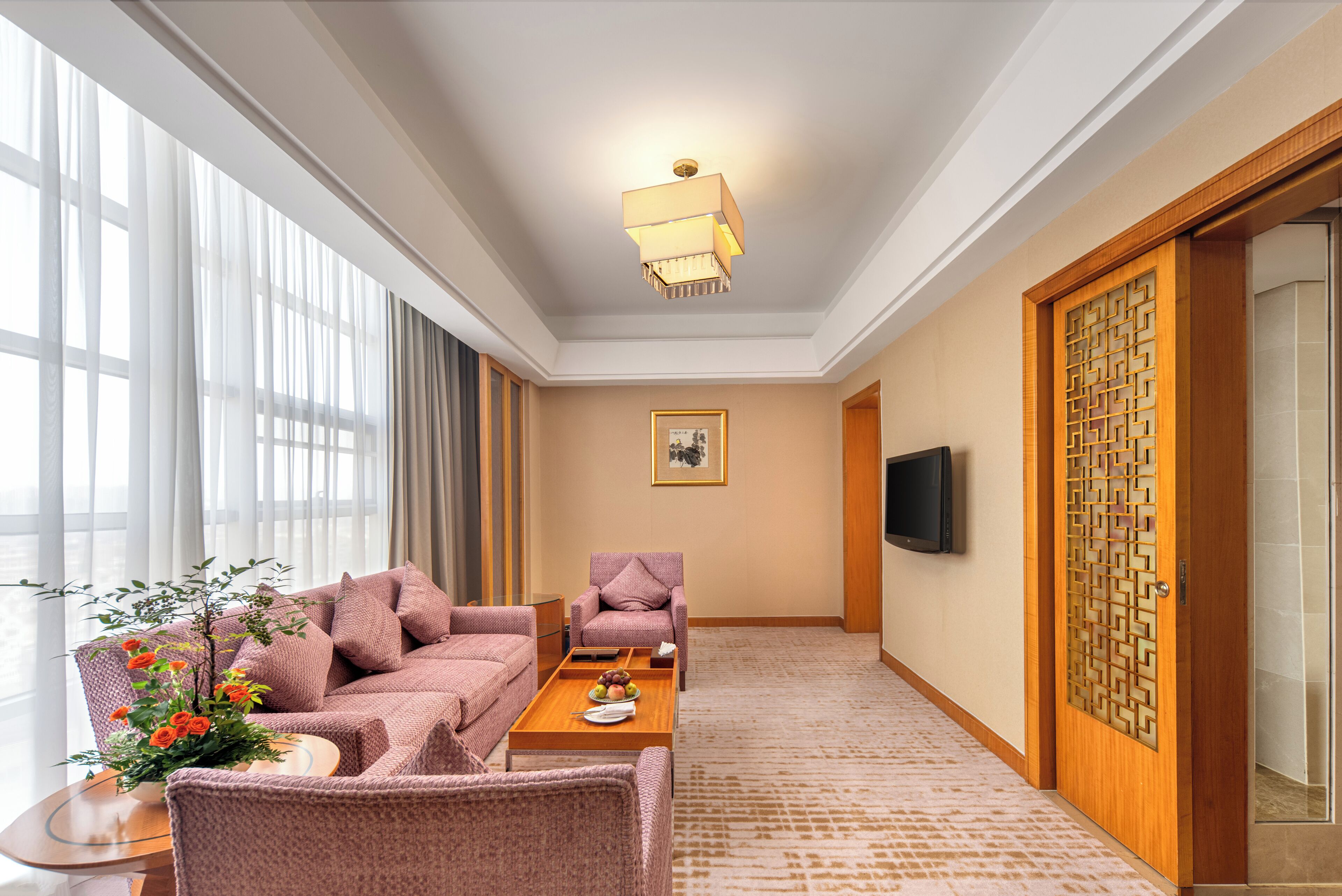 A hotel room with a sofa, armchair, and a coffee table with a tray of fruit.