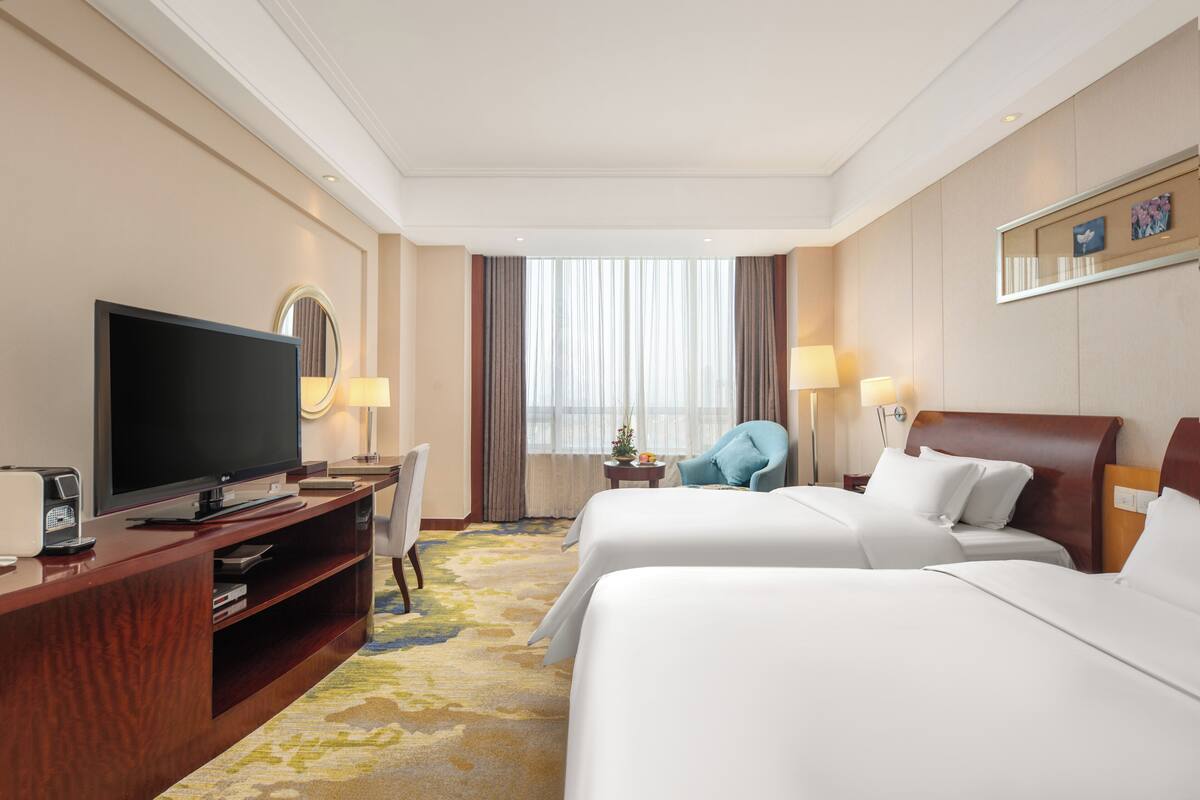 Ein Hotelzimmer mit zwei Betten, einem Fernseher, einem Schreibtisch mit Computer und einem Sessel.