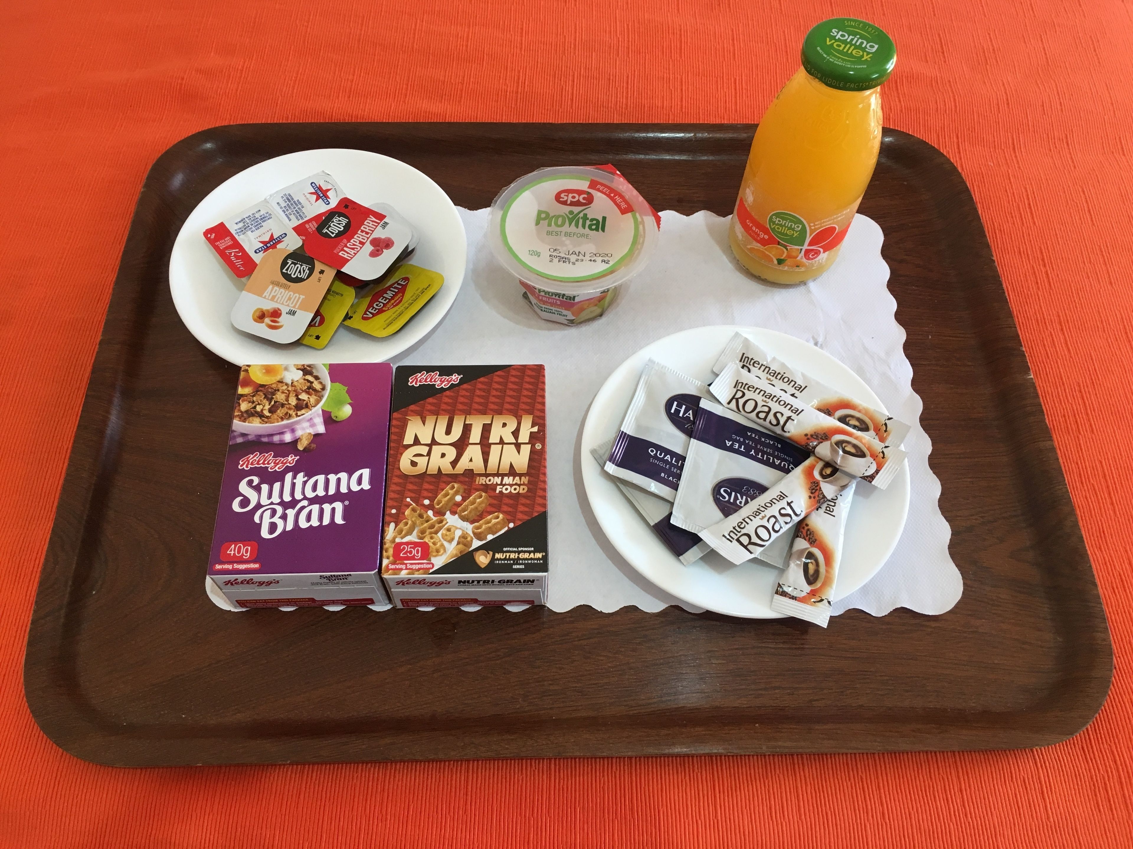 Una bandeja con diferentes alimentos, como cereal, yogur y una botella de jugo.