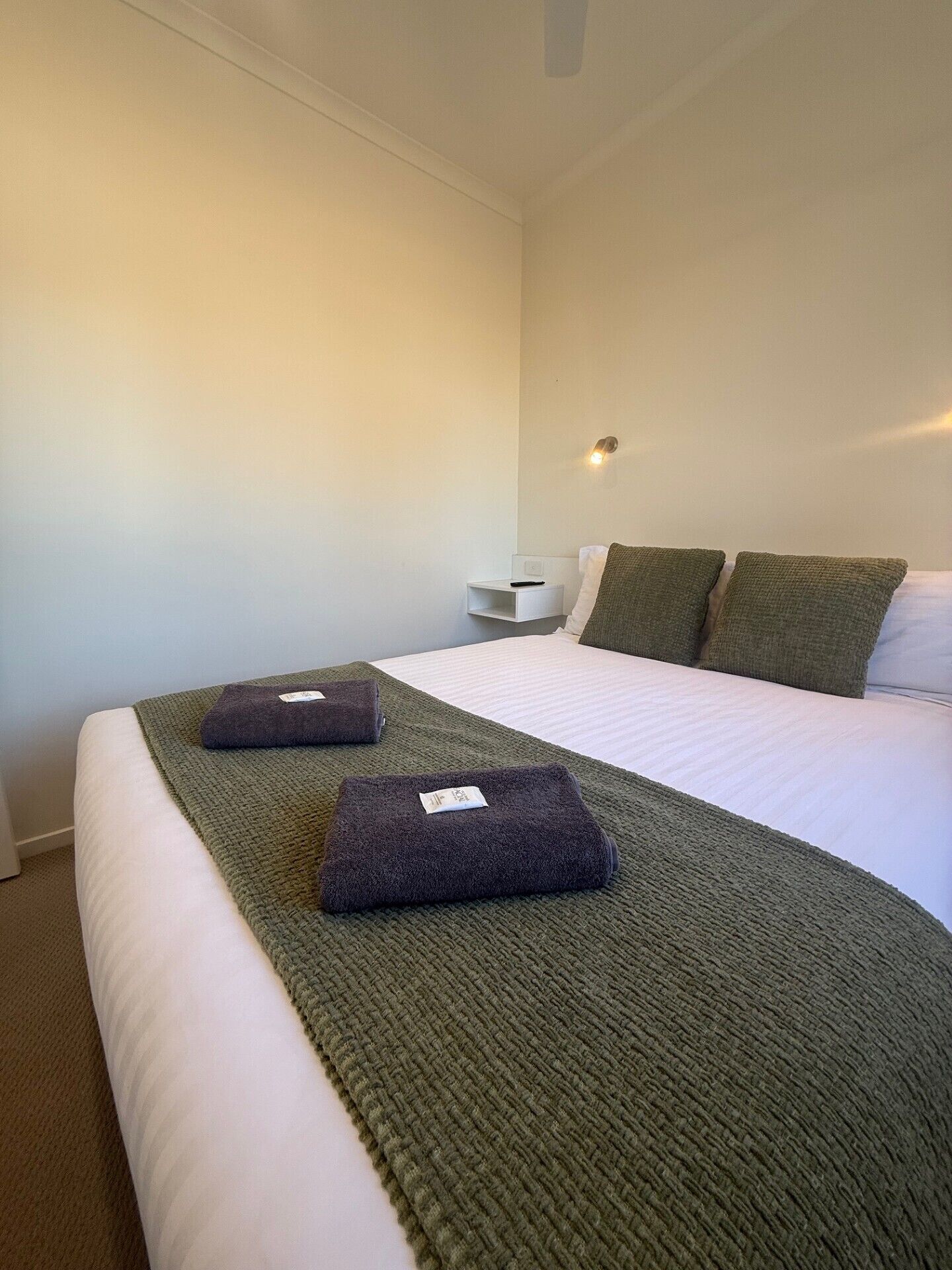 A hotel room with a neatly made bed, a bedside table with a lamp, and a wall-mounted light fixture.