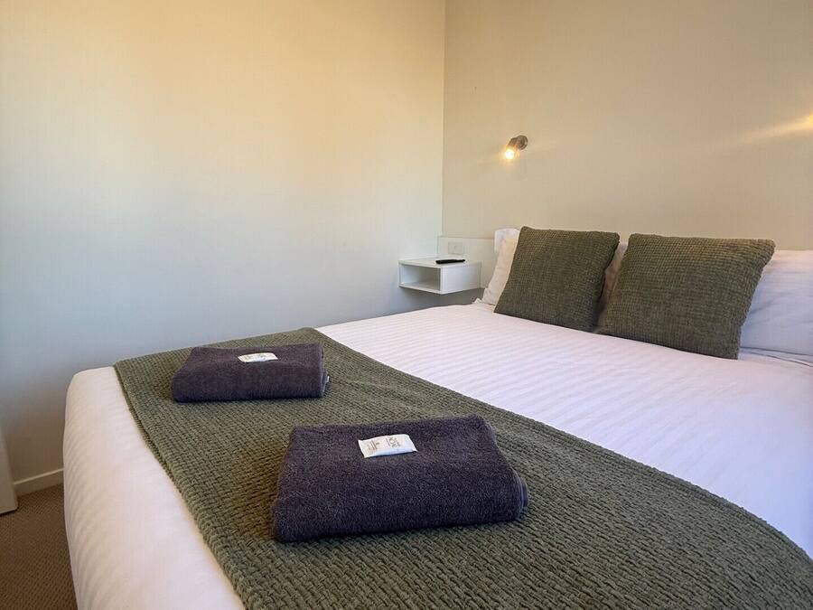 A hotel room with a neatly made bed, a bedside table with a lamp, and a wall-mounted light fixture.
