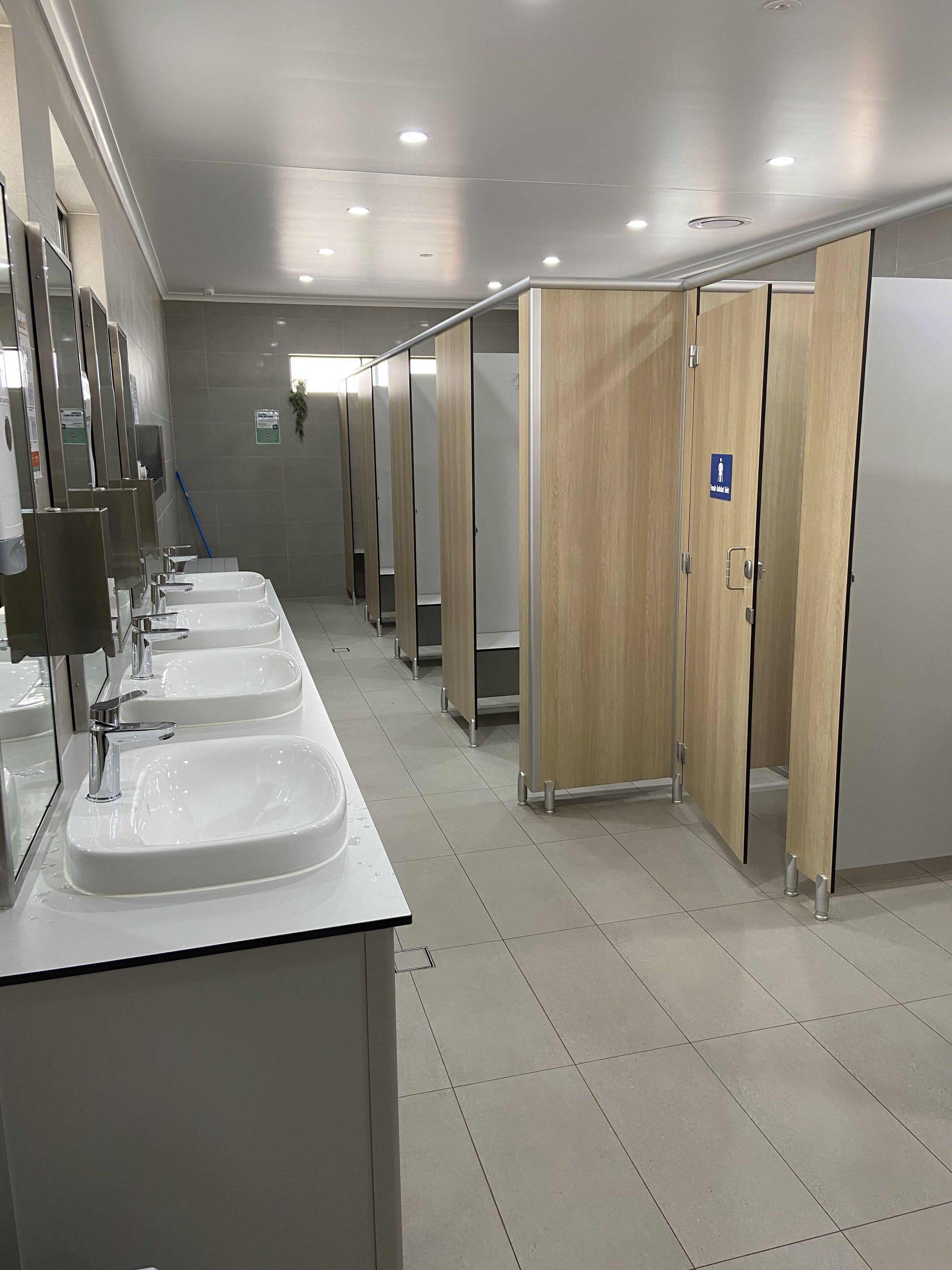 Ein sauberes, modernes Badezimmer mit mehreren Waschbecken und Holztrennwänden.