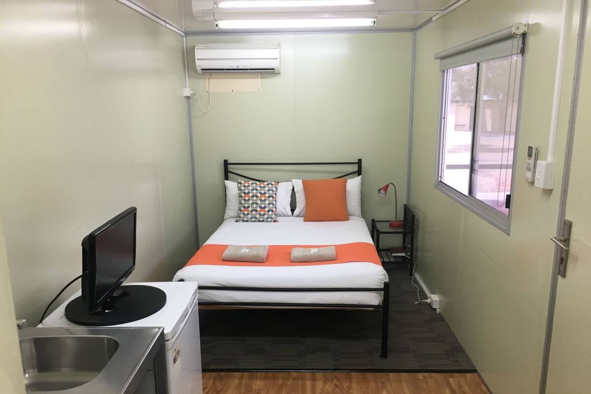 Habitación de hotel pequeña con cama, escritorio con computadora, lavamanos, aire acondicionado y ventana.