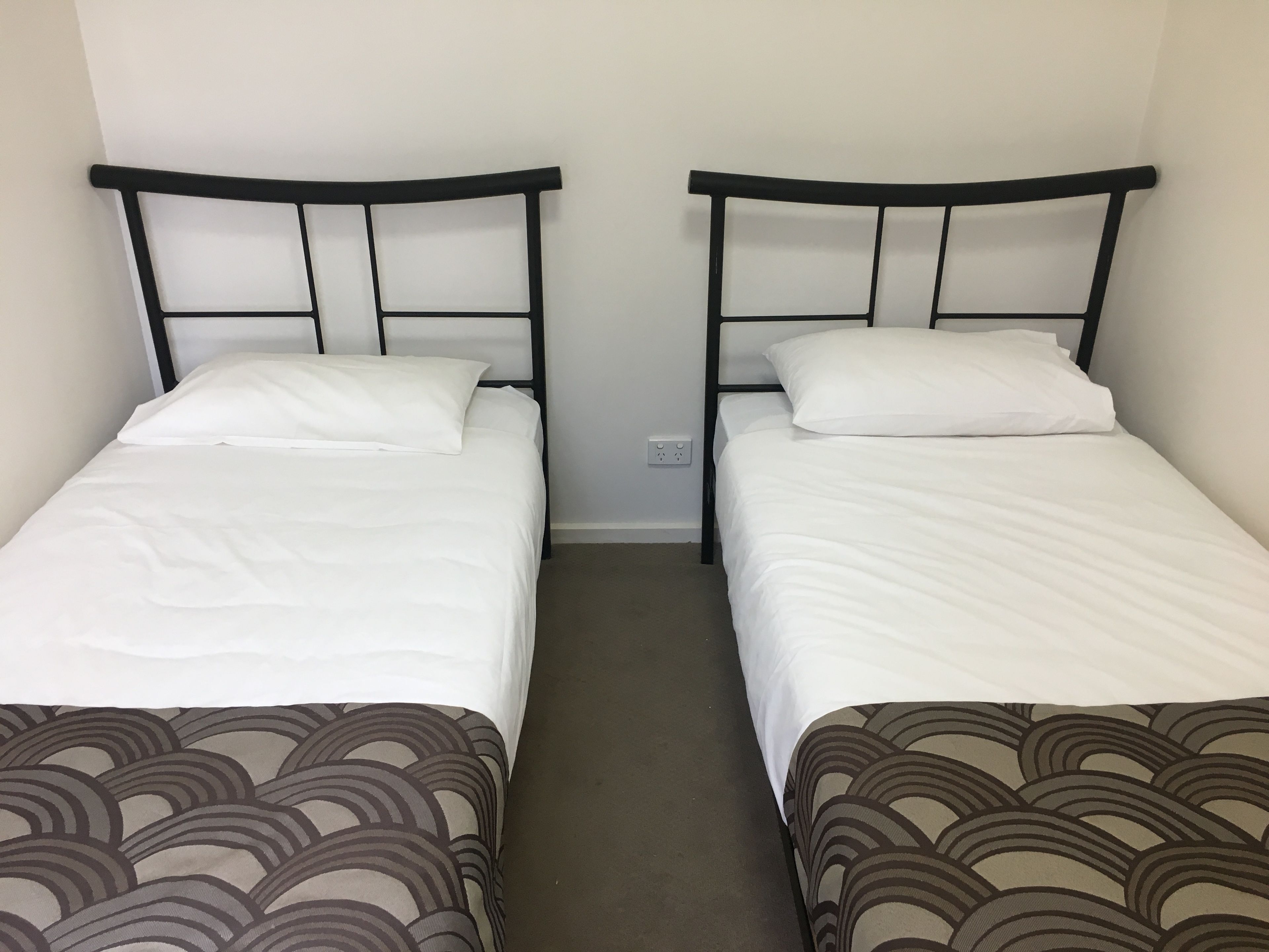 Deux lits simples avec des cadres noirs et du linge de lit blanc, séparés par un petit espace.