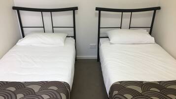 Deux lits simples avec des cadres noirs et du linge de lit blanc, séparés par un petit espace.