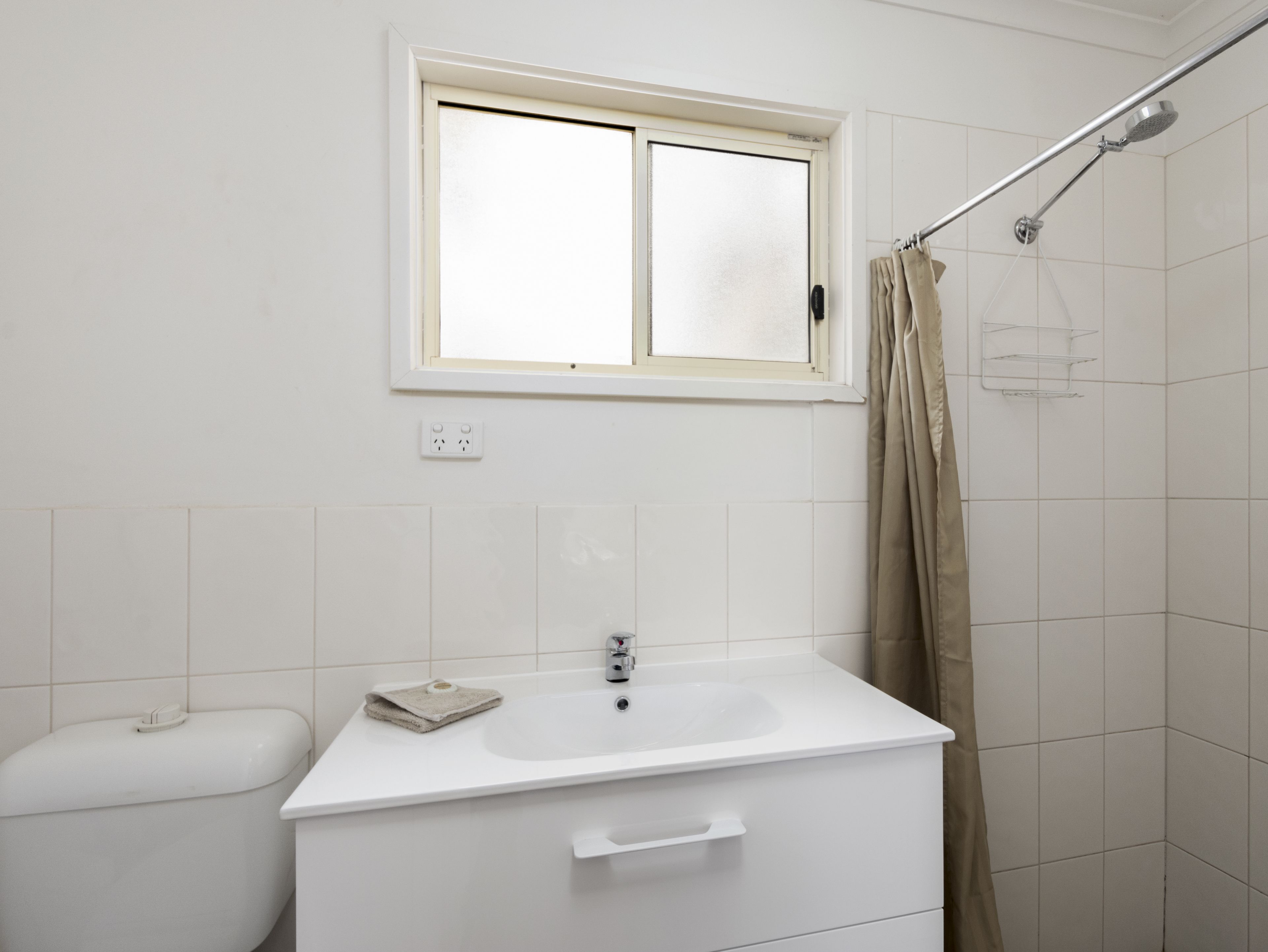 A bathroom with a white sink, a window above the sink, a shower with a curtain, and a toilet.