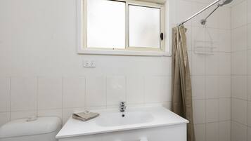 A bathroom with a white sink, a window above the sink, a shower with a curtain, and a toilet.