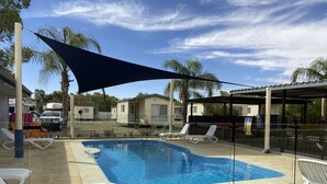Una piscina con sillones de descanso, una zona sombreada y casas móviles al fondo.
