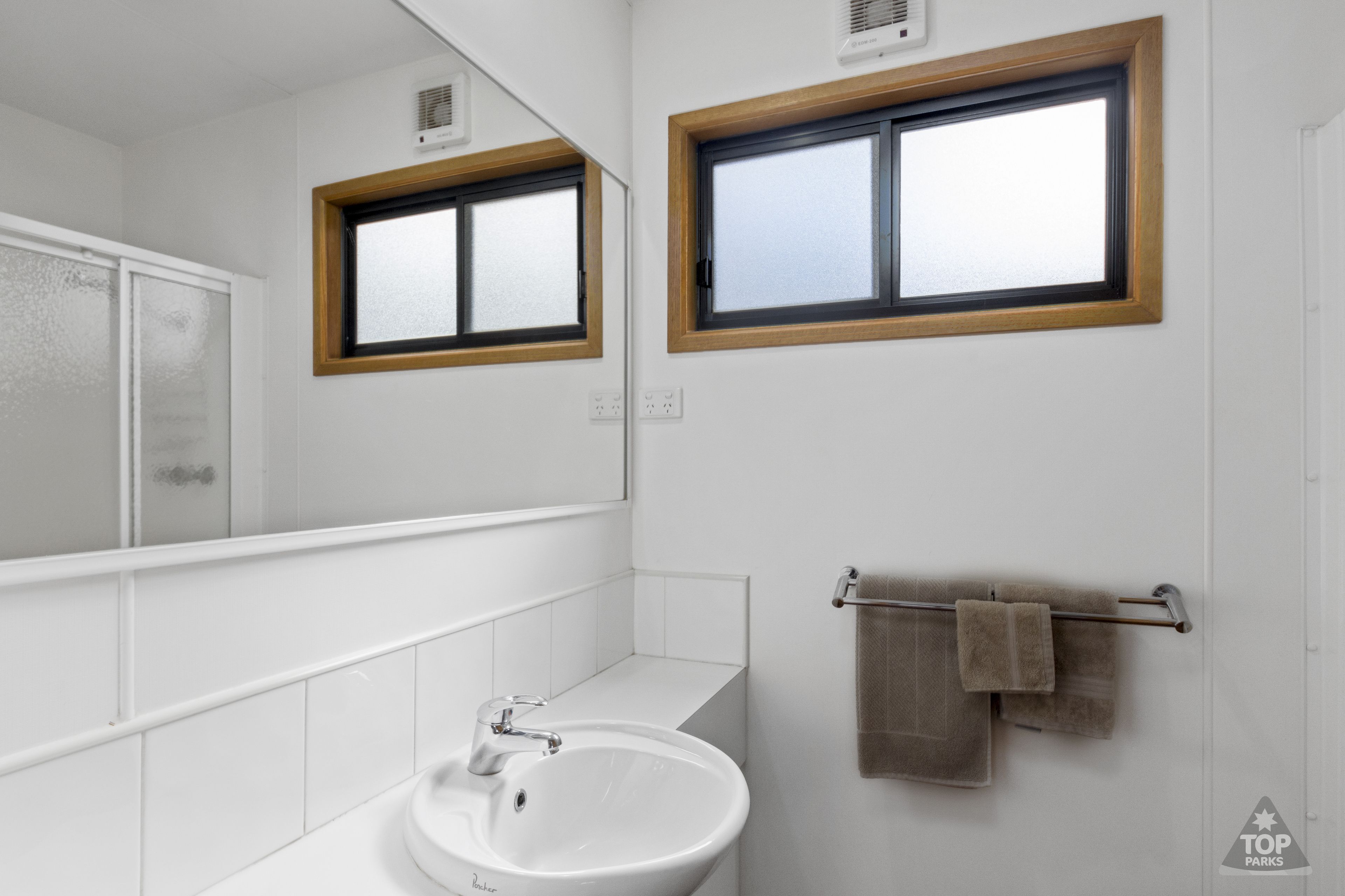 Een badkamer met een witte wastafel, een spiegel en een handdoekrek met handdoeken.