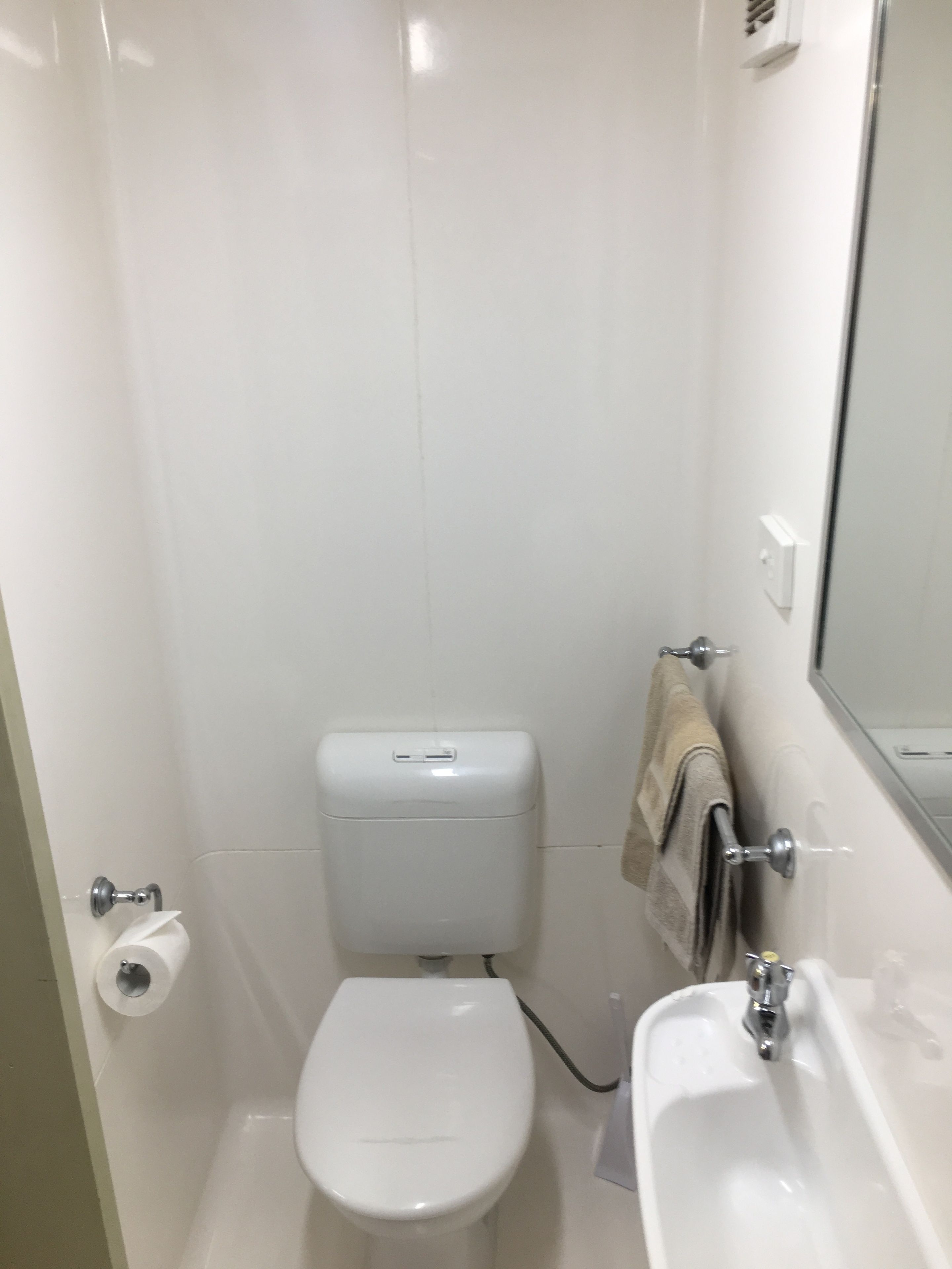 A small, white bathroom with a toilet, a sink, and a towel hanging on the wall.