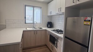 Una cocina moderna con armarios blancos, un refrigerador de acero inoxidable, horno empotrado y una ventana con persianas.