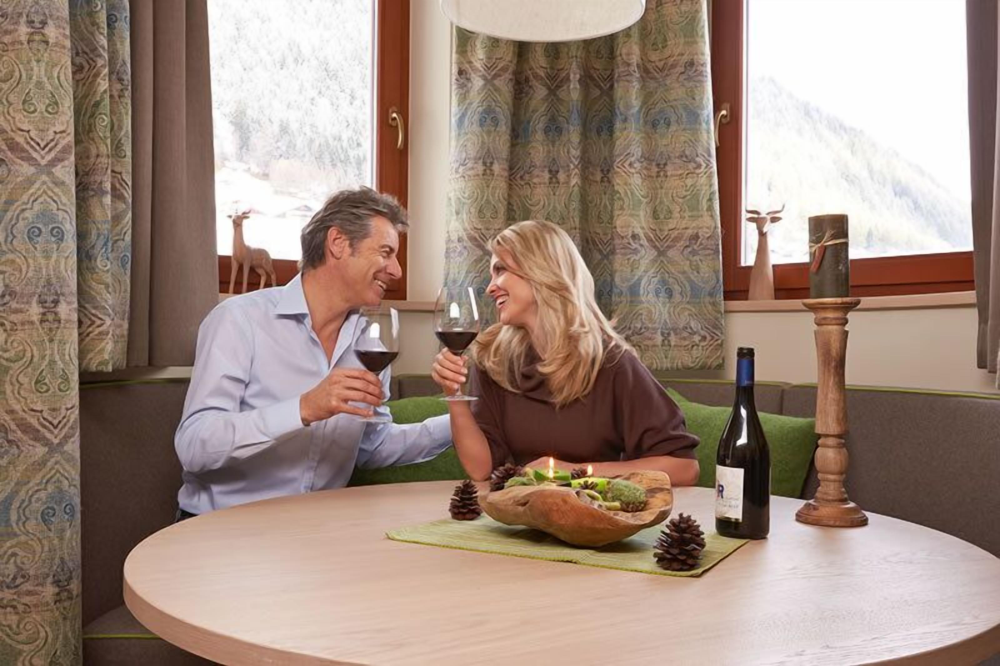 A couple seated at a round table with a wooden bowl centerpiece, a bottle of wine, and a candle.