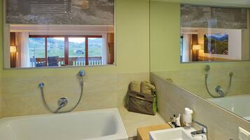 A bathroom with a bathtub, a sink, and a window with a view of a house and landscape.