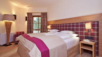 A neatly made bed with a plaid headboard, a bedside table with a lamp, and a window with curtains.