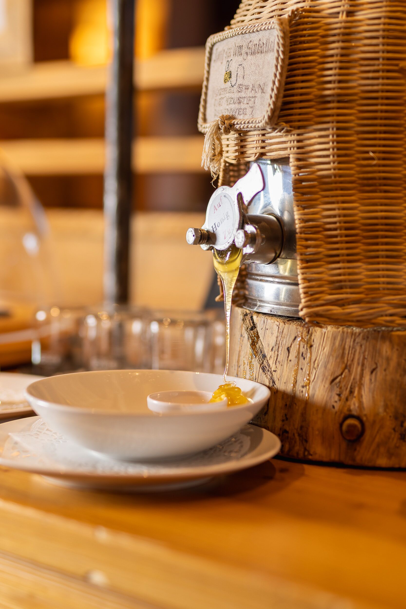 A wooden barrel with a metal tap dispensing honey into a white bowl.