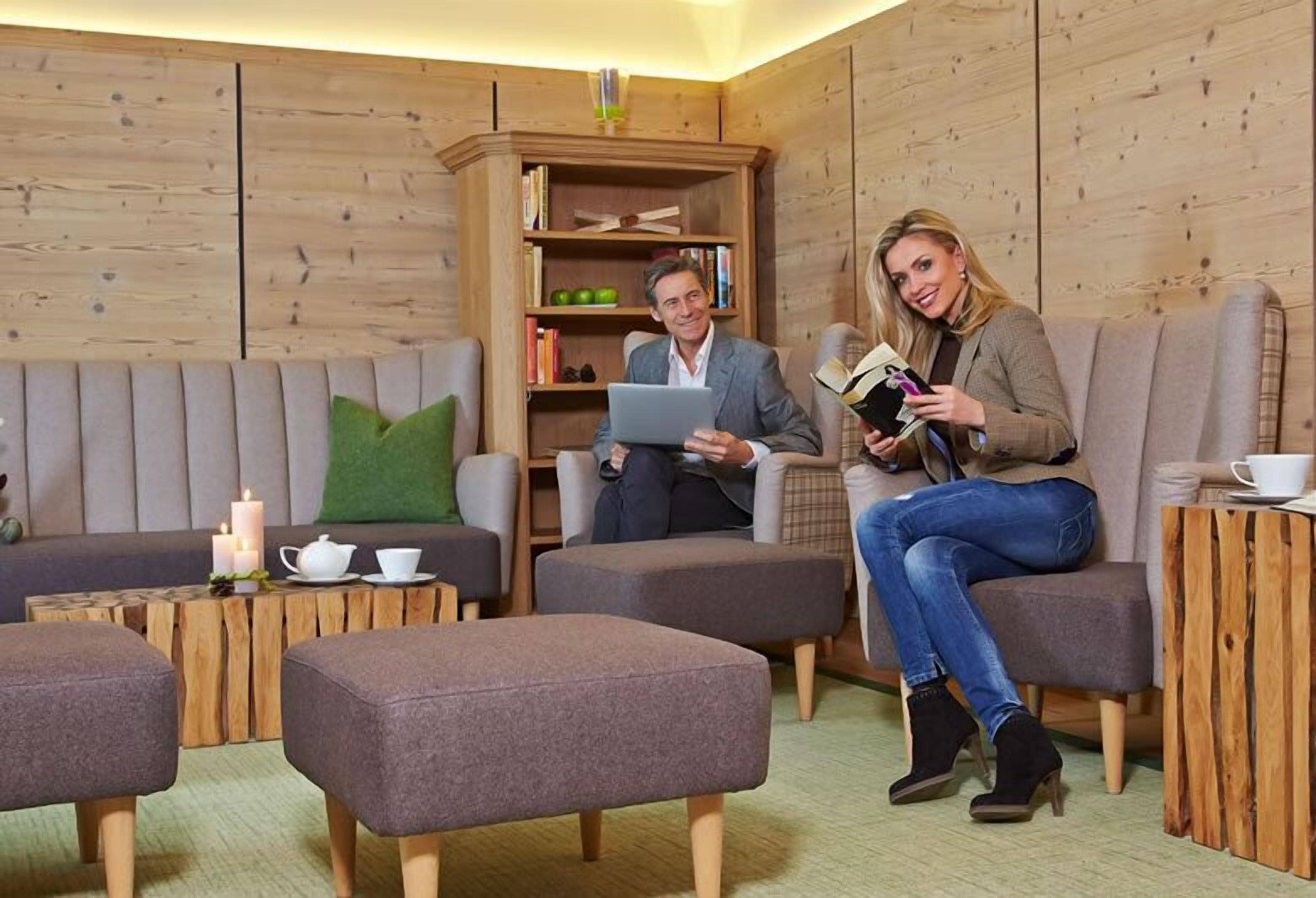 Una habitación acogedora con un sofá, dos otomanas, una estantería de madera y una computadora portátil.
