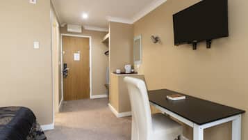 A hotel room with a bed, a desk, a chair, a television, and a shower area.