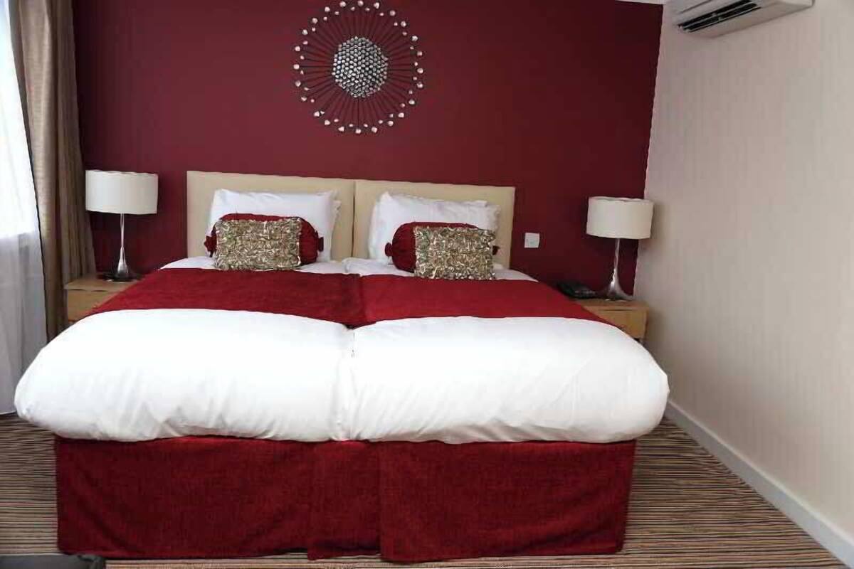 A hotel room with a large bed, two bedside tables, a wall-mounted air conditioner, and a decorative wall piece.