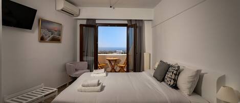 A hotel room with a large bed, a TV, a painting, a balcony with a view, and a small table with chairs.