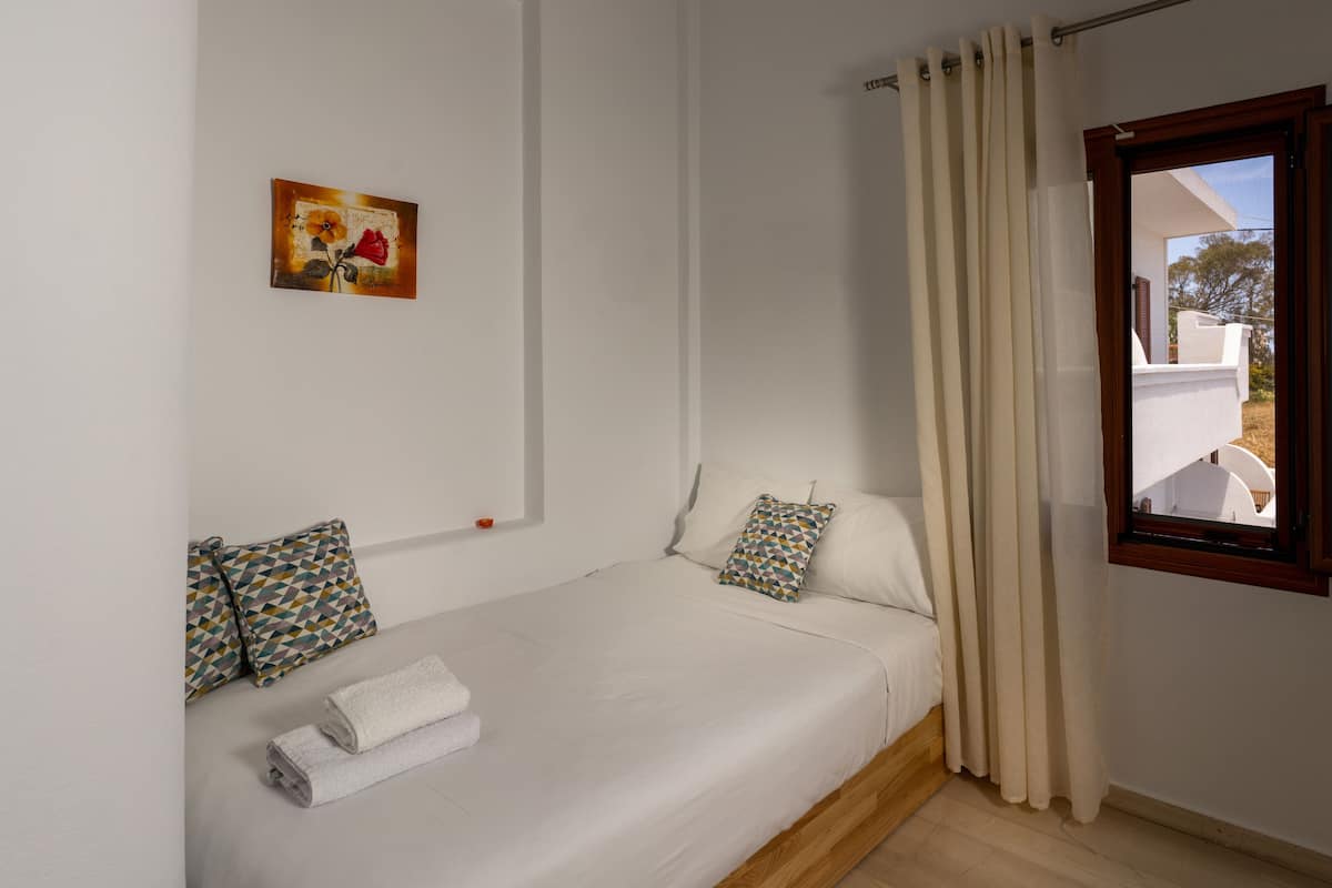 A single bed with a white mattress, two pillows, a folded towel, and a painting on the wall.