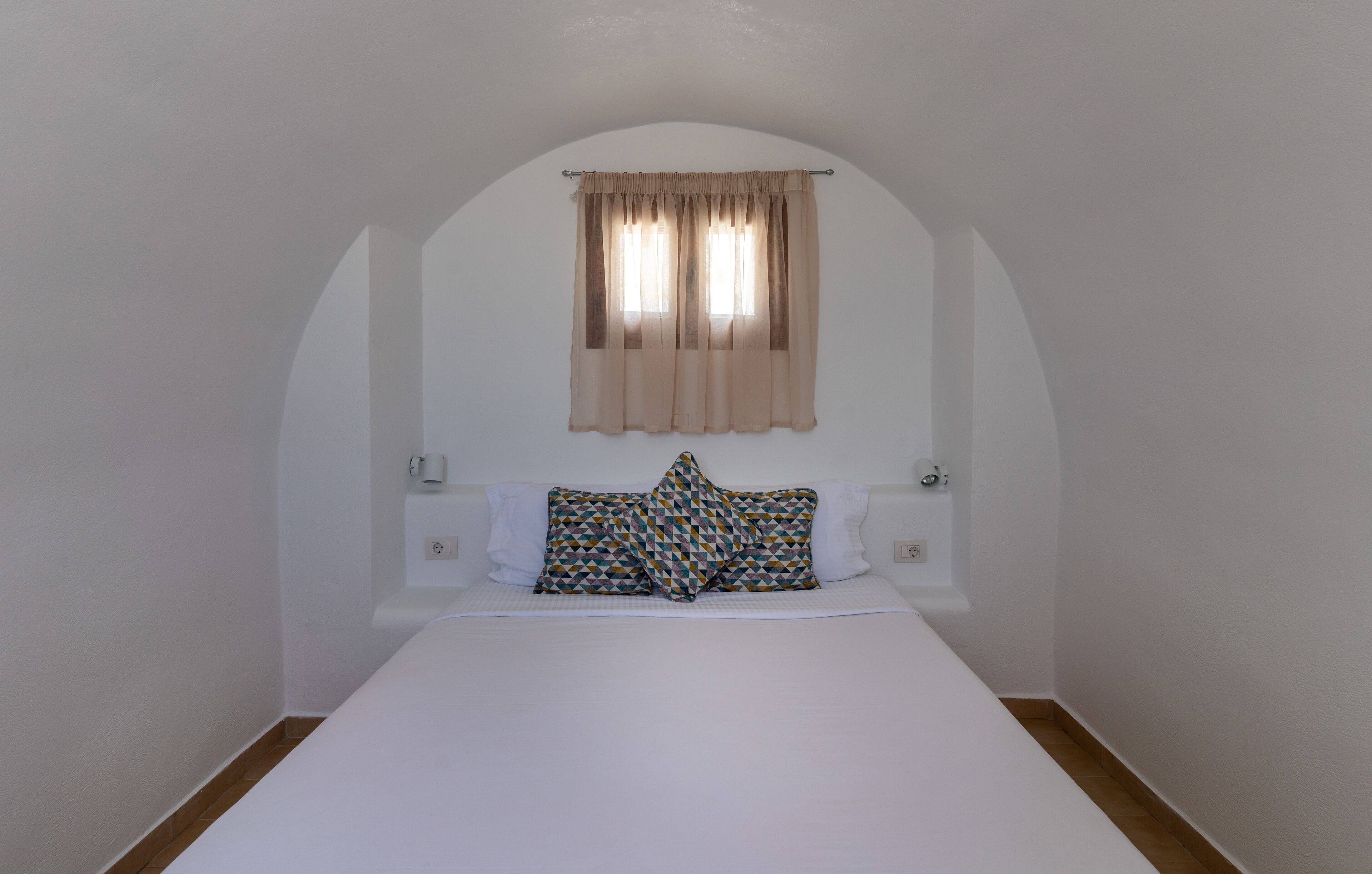 Une petite pièce avec un lit simple, une fenêtre avec des rideaux et un luminaire fixé au mur.