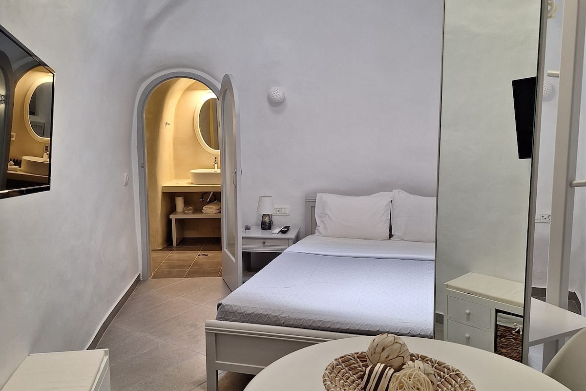 A modern, minimalist bedroom with a bed, bedside table, and a round table with a basket.
