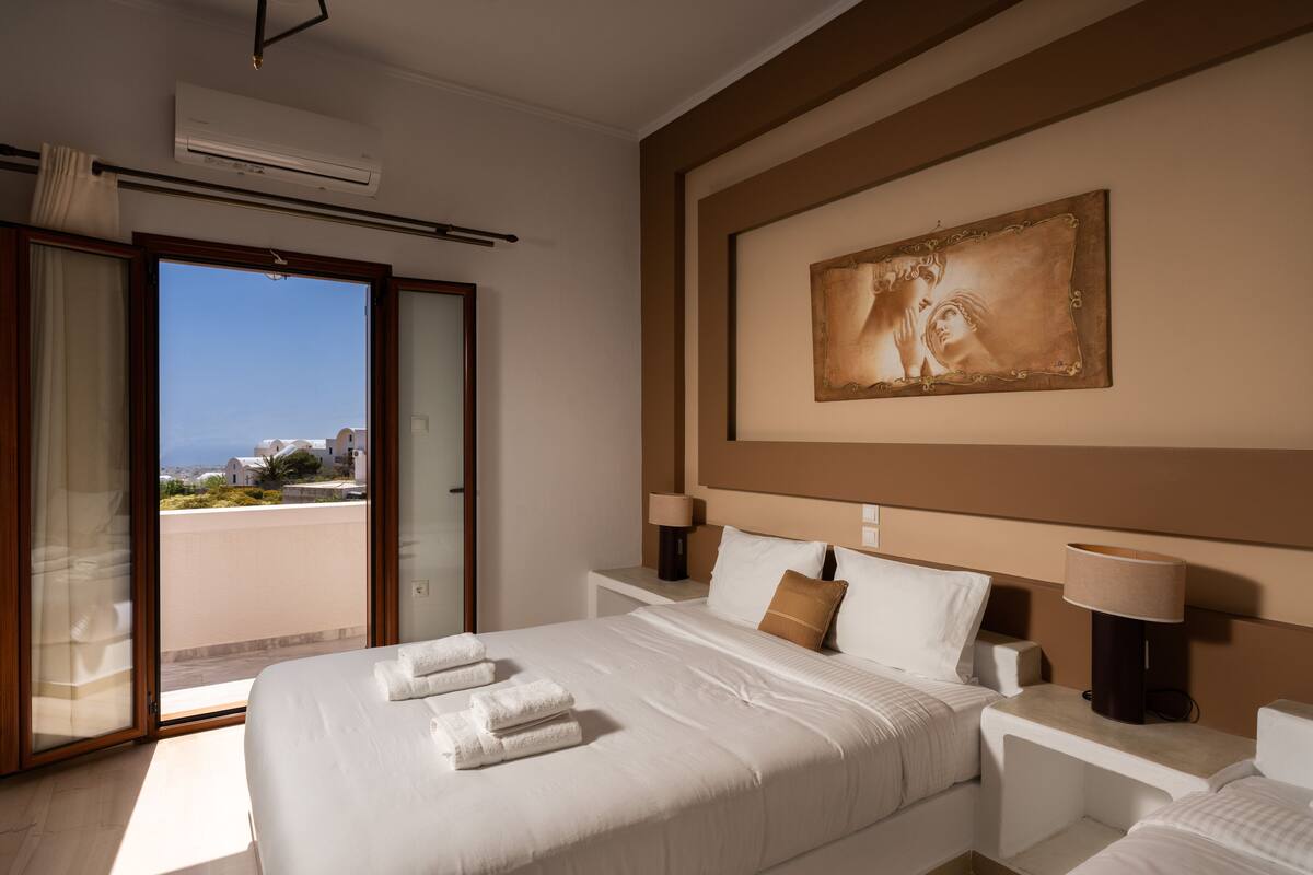 A hotel room with a bed, two bedside tables, a large window, and a painting on the wall.
