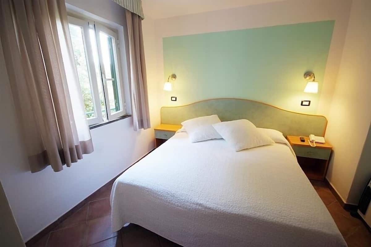 Une chambre d’hôtel comprenant un lit, deux tables de chevet, une fenêtre avec des rideaux et des lampes fixées au mur.
