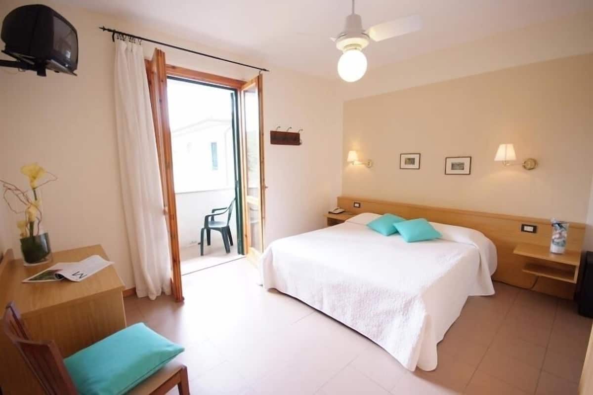 Une chambre d’hôtel comprenant un lit, un bureau avec une chaise, une télévision, un ventilateur de plafond et une porte coulissante donnant sur le balcon.